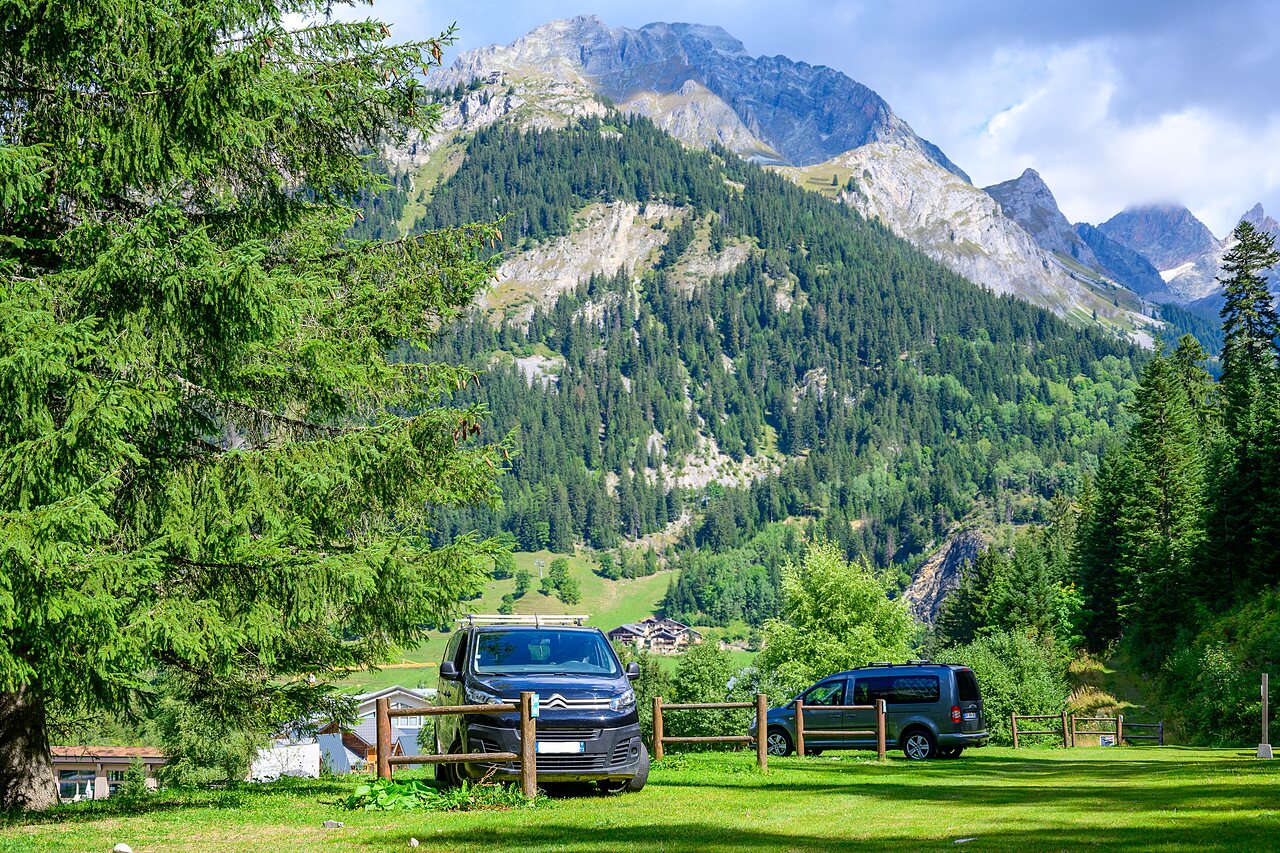 Vans gar�s sur terrain herbeux avec montagnes et for�t au camping CLICOCHIC Alpes Lodges � Pralognan la Vanoise (73).