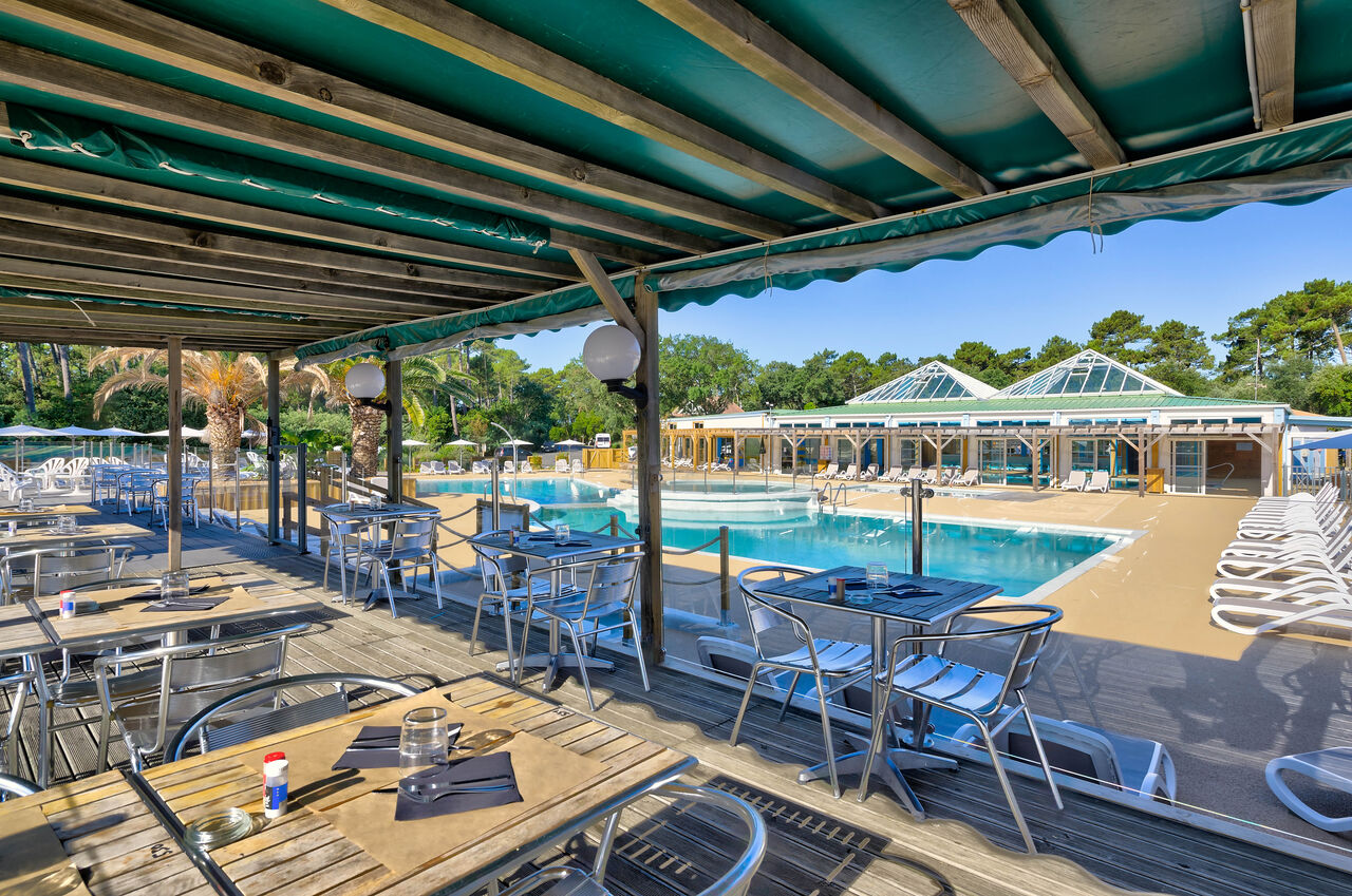 Terrasse de restaurant ombrag�e avec vue sur la grande piscine ext�rieure au camping LIBRANOO Naturiste Arnaoutchot � Veille-Saint-Girons, Landes, France.