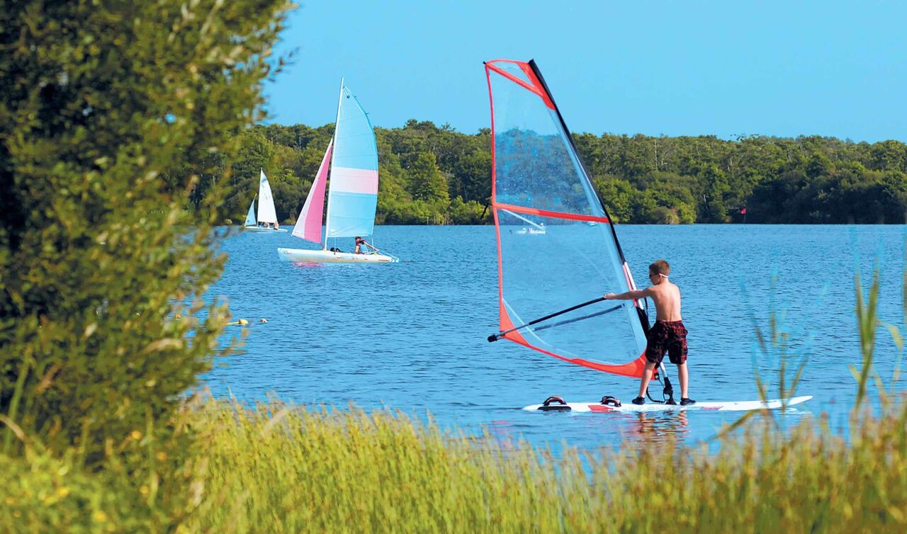 Jeune en planche � voile et voiliers sur lac au camping LIBRANOO Naturiste Arnaoutchot, Landes, France.