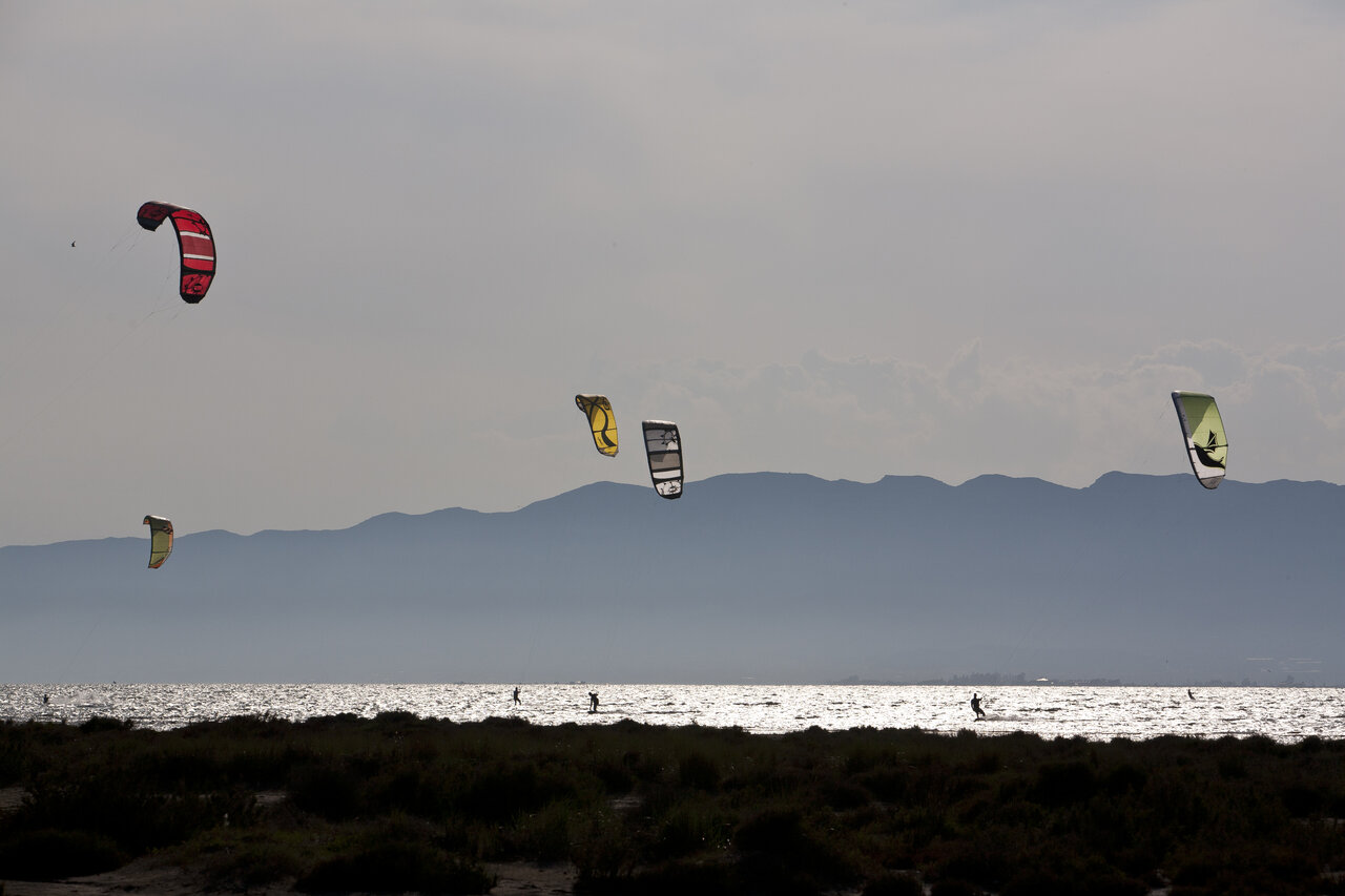 Kitesurfers sur l'eau scintillante avec montagnes au camping CAPFUN Aube � Deltebre, Tarragone.