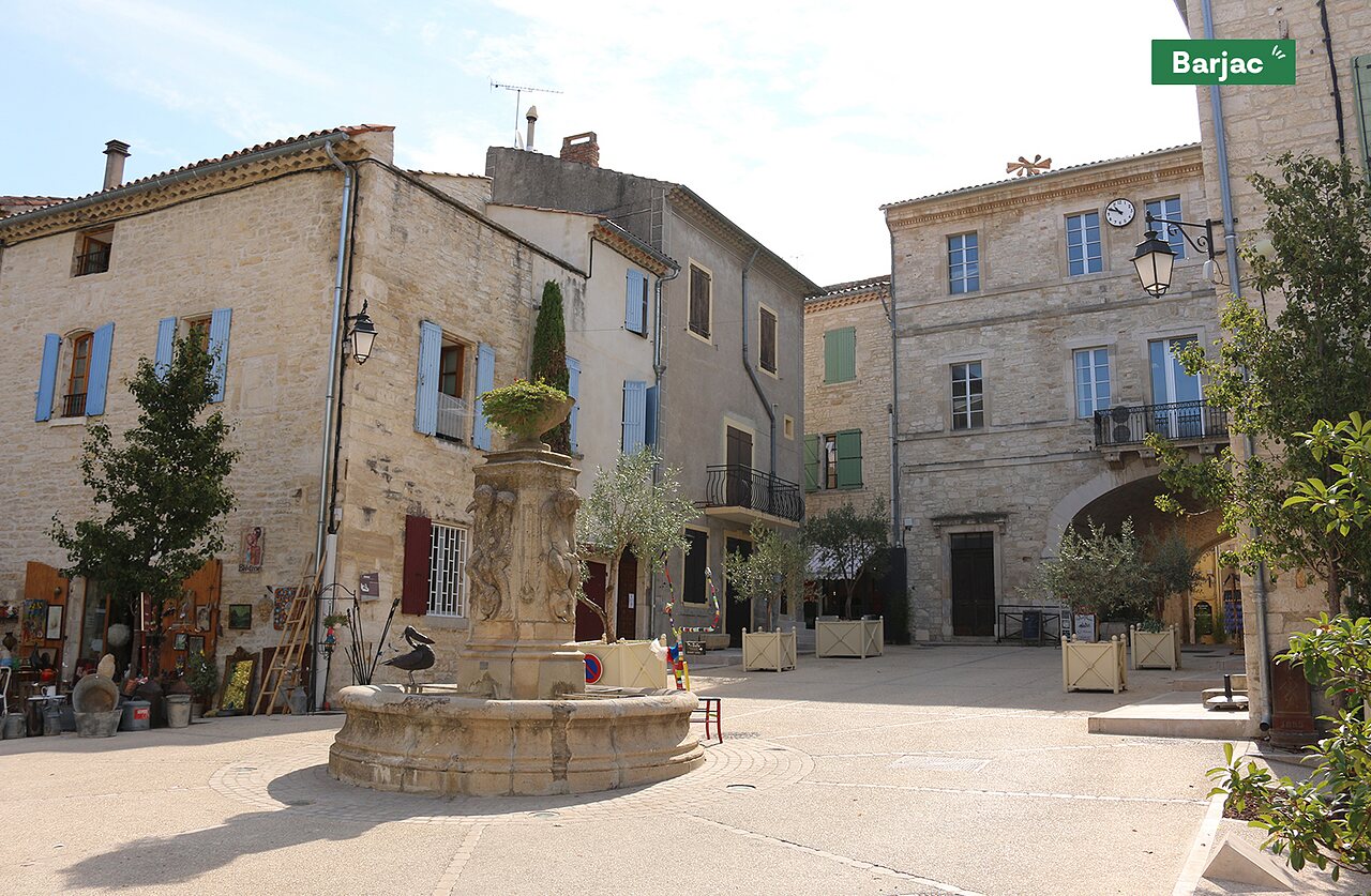 Place du village de Barjac avec fontaine historique et b�timents en pierre.