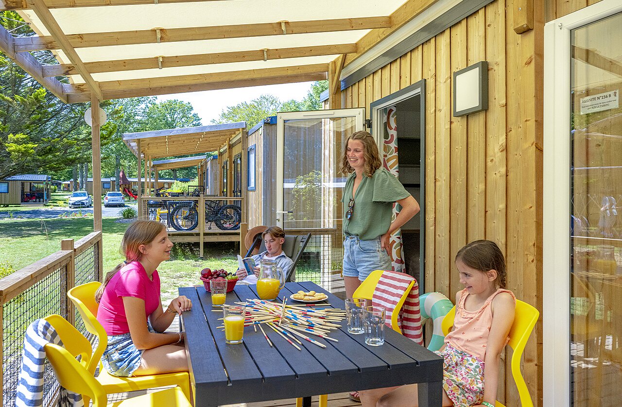Famille profitant de la terrasse couverte d'un mobile home avec jeu au camping CAPFUN Ch�teau de Galin�e � SAINT CAST LE GUILDO (22).