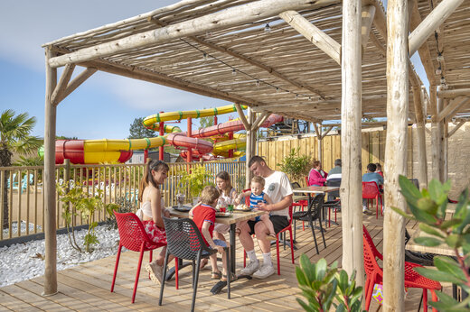 Famille d�jeunant en terrasse du restaurant, toboggans aquatiques au camping CAPFUN Chateau d'Arvid (14).
