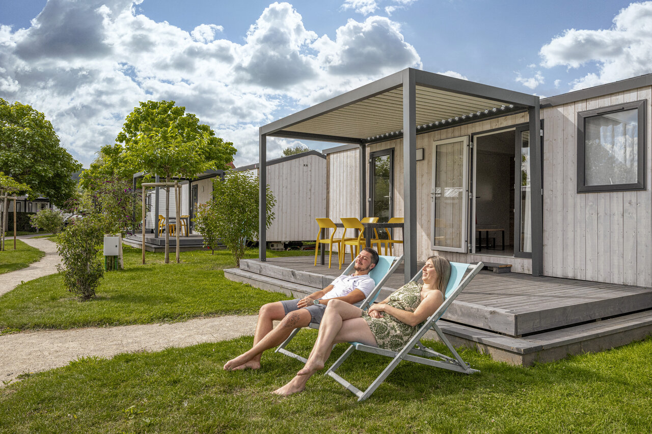 Mobile-home moderne avec terrasse et couple relaxant au camping CLICOCHIC Chevaliers � HOULGATE (14).