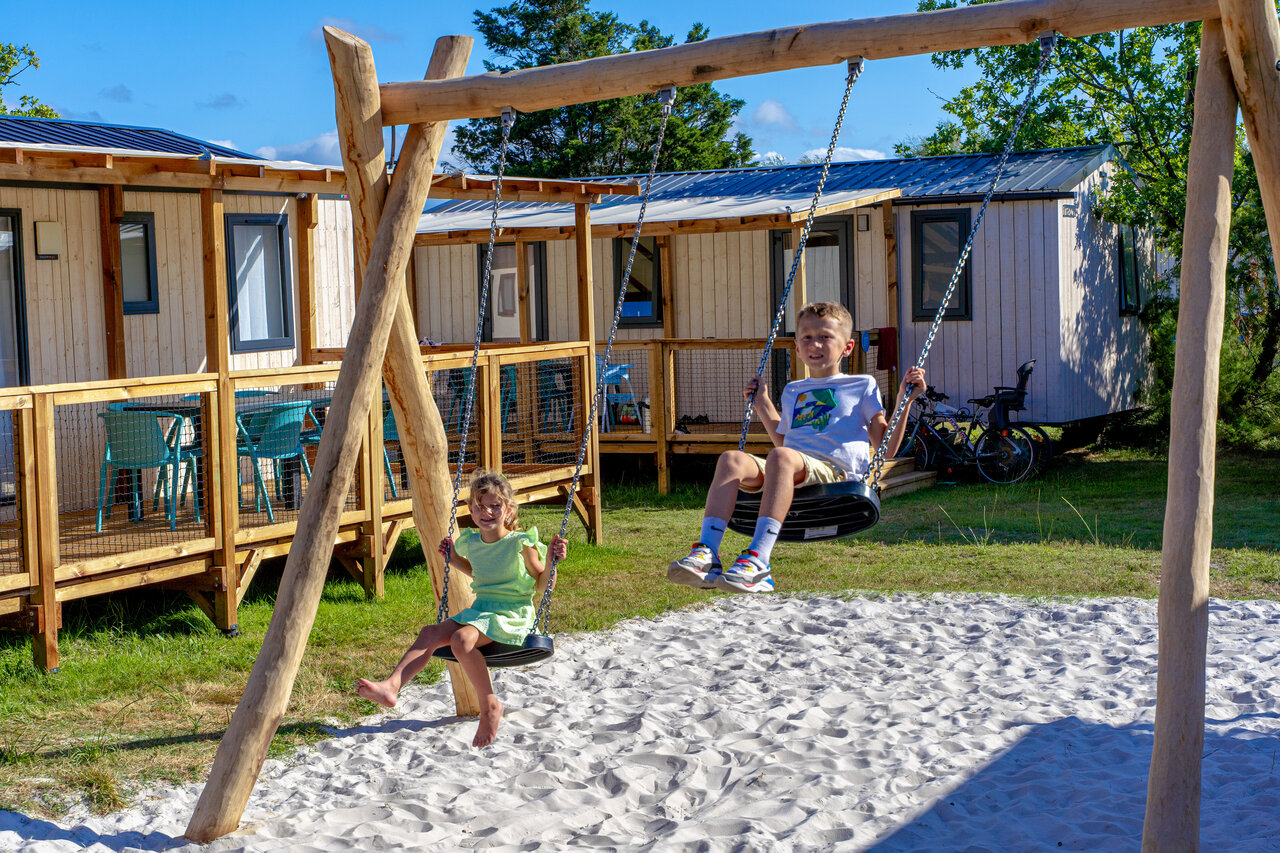 Enfants jouant sur une balan�oire en bois devant des mobile-homes au camping VAGUES OCEANES Coq Hardi � Cassy-Lanton (33).