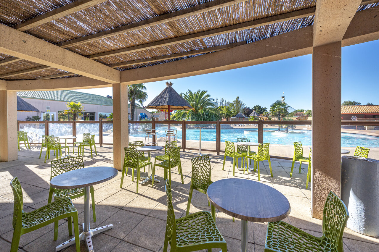 Terrasse ombrag�e du bar avec tables et chaises vertes, pr�s de la piscine, au camping CAPFUN Dauphins Bleus � GIVRAND (85).