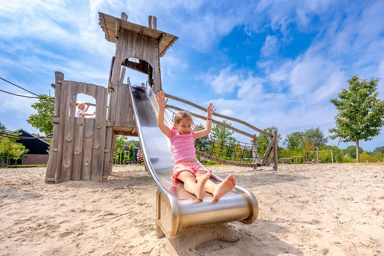 Enfants jouant sur un toboggan et une structure en bois au camping CAPFUN De Belten � Rheeze.