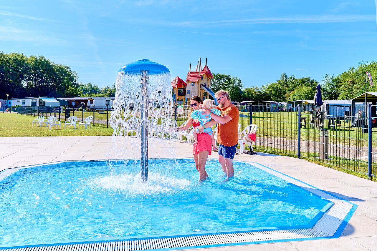 Famille avec b�b� dans pataugeoire avec champignon d'eau, aire de jeux au camping CAPFUN De Eikenhof � Paasloo/Oldemarkt.