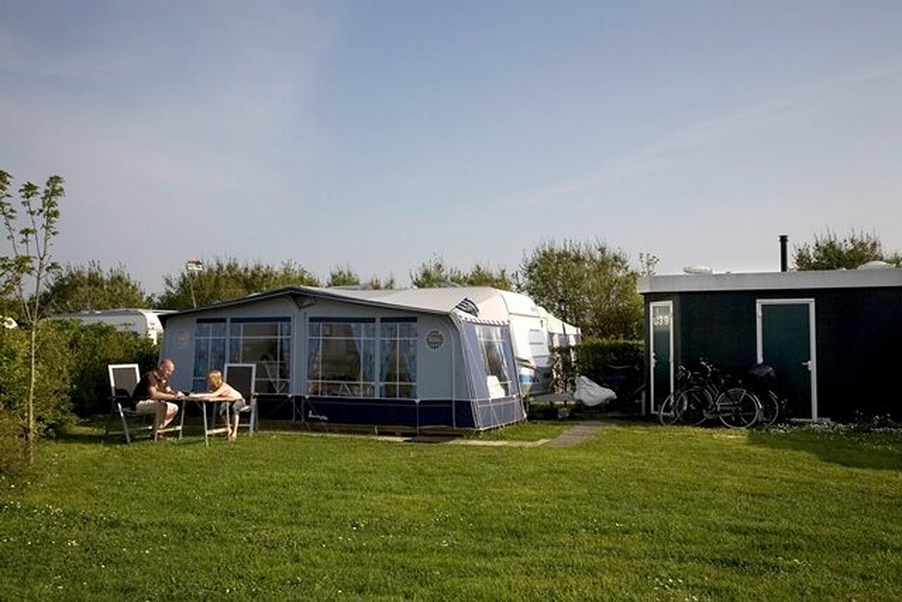 Caravane avec auvent, couple sur terrain herbeux au camping CAPFUN De Pekelinge � Oostkapelle.