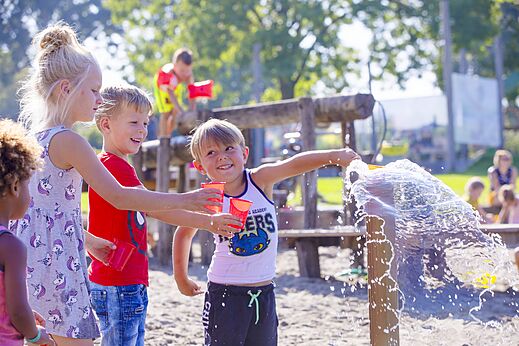 Enfants joyeux jouant avec de l'eau et des gobelets dans l'aire de jeux au camping CAPFUN De Rotonde � Enspijk.