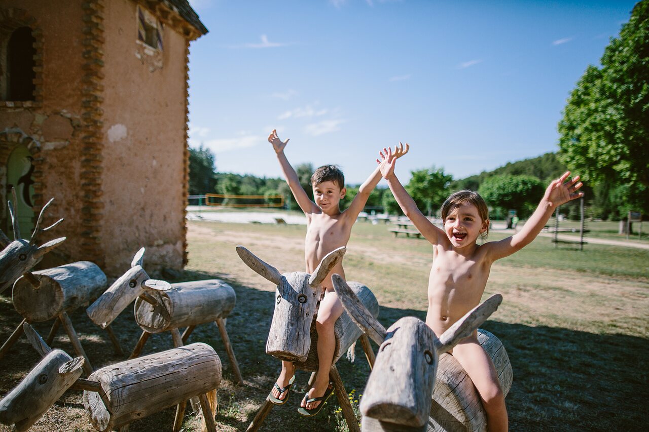 Enfants naturistes sur animaux en bois � l'aire de jeux au camping LIBRANOO Naturiste Belezy � B�doin (84).