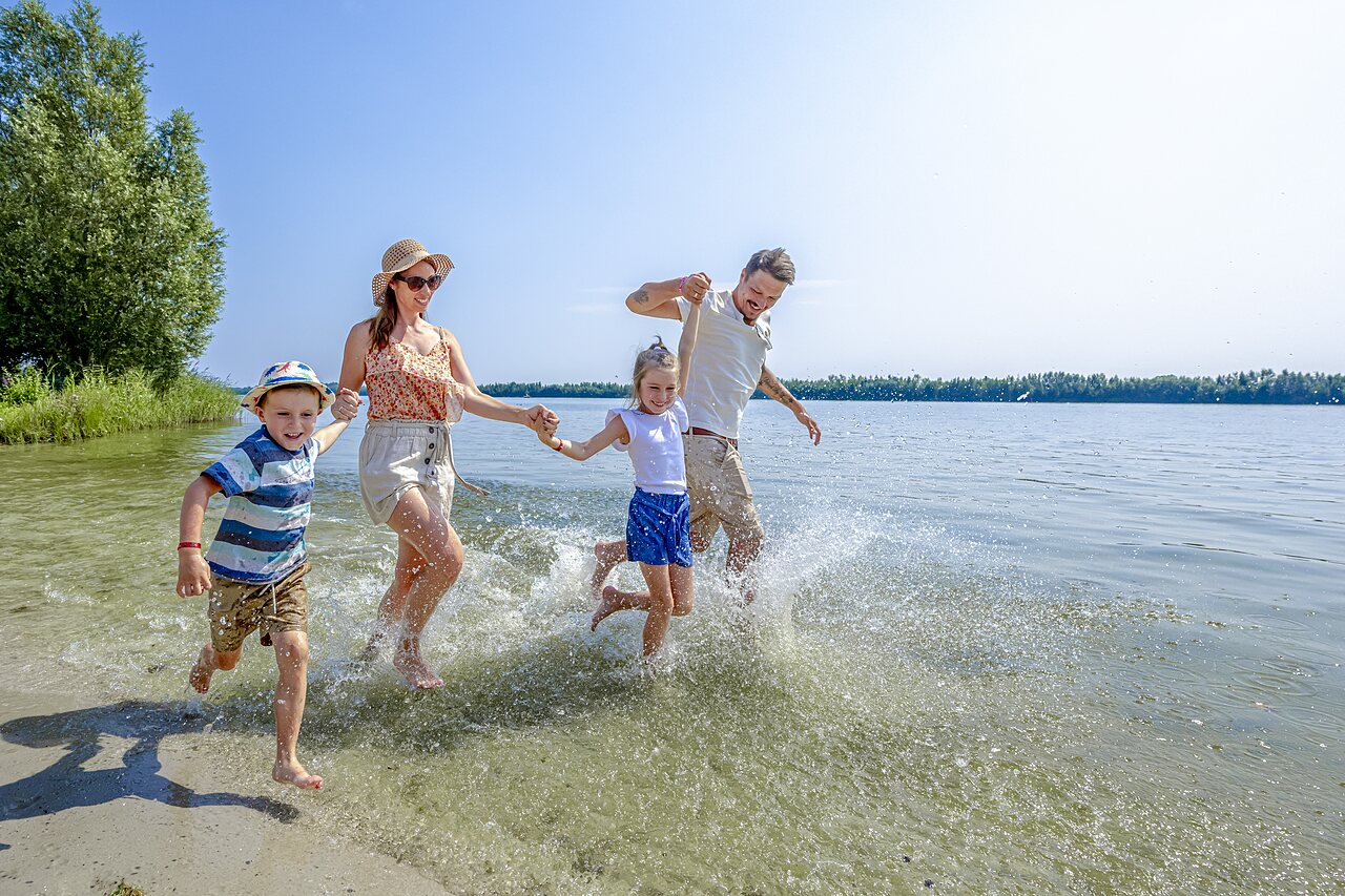 Famille joyeuse courant et �claboussant dans l'eau peu profonde au camping CAPFUN Erkemederstrand � Zeewolde.