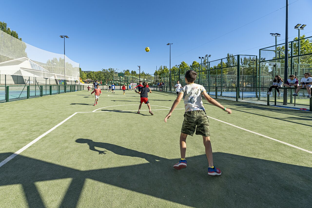 Enfants jouant au football sur terrain multisport au camping CAPFUN El Escorial, Madrid.