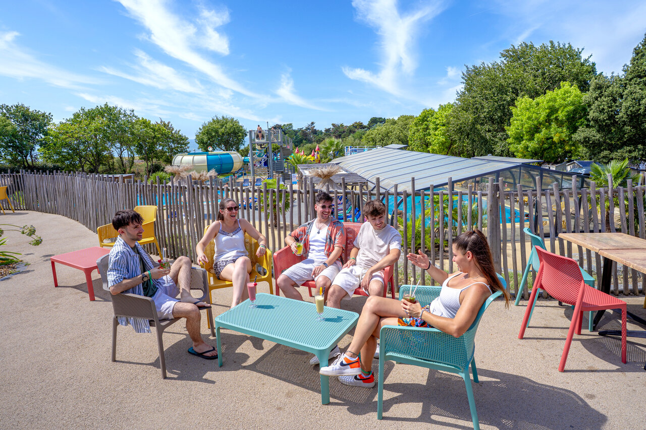 Groupe d'amis au bar ext�rieur avec toboggans aquatiques et piscine au camping CAPFUN L'Eve � Saint-Marc-sur-Mer (44).