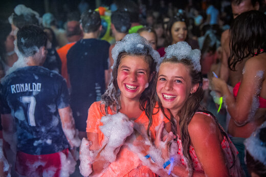 Deux jeunes filles souriantes profitant d'une soirée mousse animée au camping CAPFUN Fredland à Tournan en Brie (77).