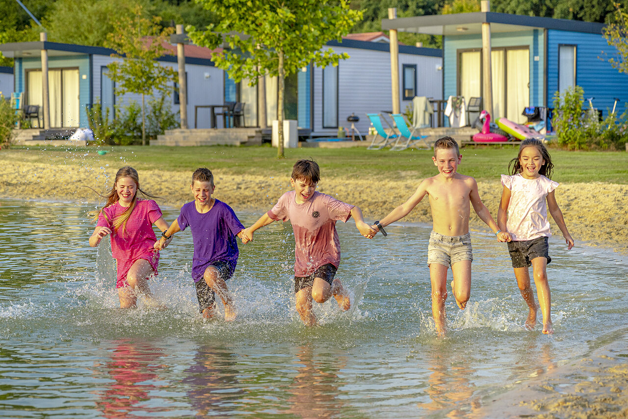 Enfants joyeux courant dans l'eau peu profonde devant des mobile-homes au camping CAPFUN De Fruithof � Klijndijk.