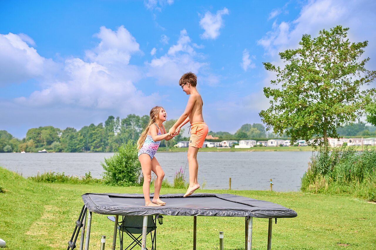 Deux enfants sautant sur un trampoline ext�rieur pr�s du lac au camping CAPFUN Groene Eiland � Appeltern.