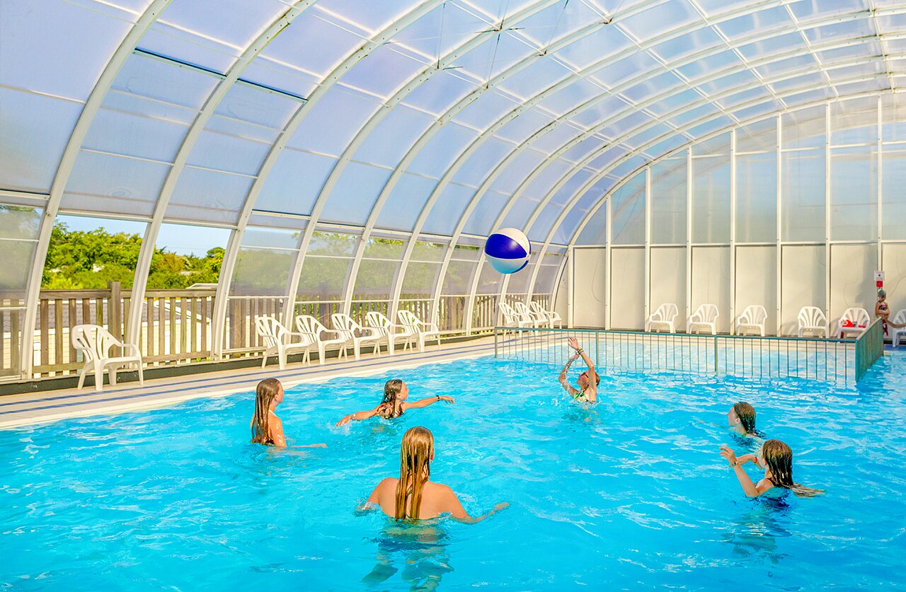 Enfants jouant au ballon dans la piscine couverte au camping VAGUES OCEANES Grosses Pierres.