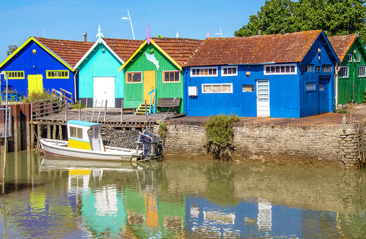 Cabanes ostréicoles colorées et bateau de pêche dans un village typique en Charente-Maritime.