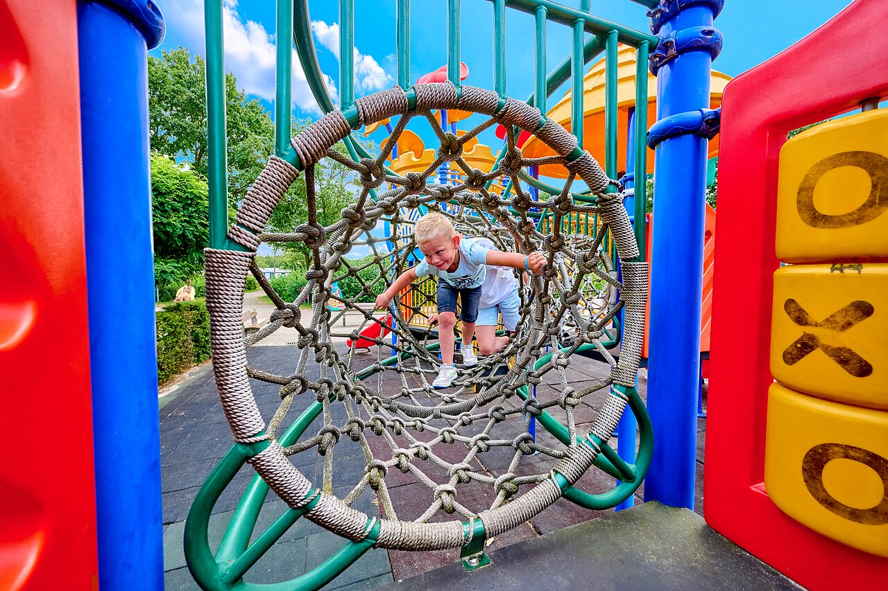 Enfant souriant dans tunnel en filet sur aire de jeux au CAPFUN Heino.