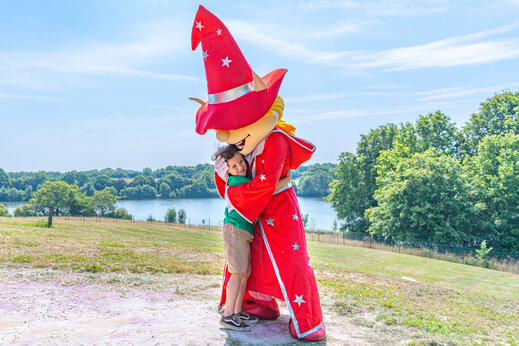 Enfant souriant étreignant la mascotte du camping lors d'une animation au camping CAPFUN Lac de Ribou à Cholet (49).