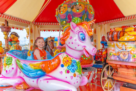 Petite fille souriante sur un man�ge licorne color� au camping VAGUES OCEANES Licorne � Dunkerque (59).