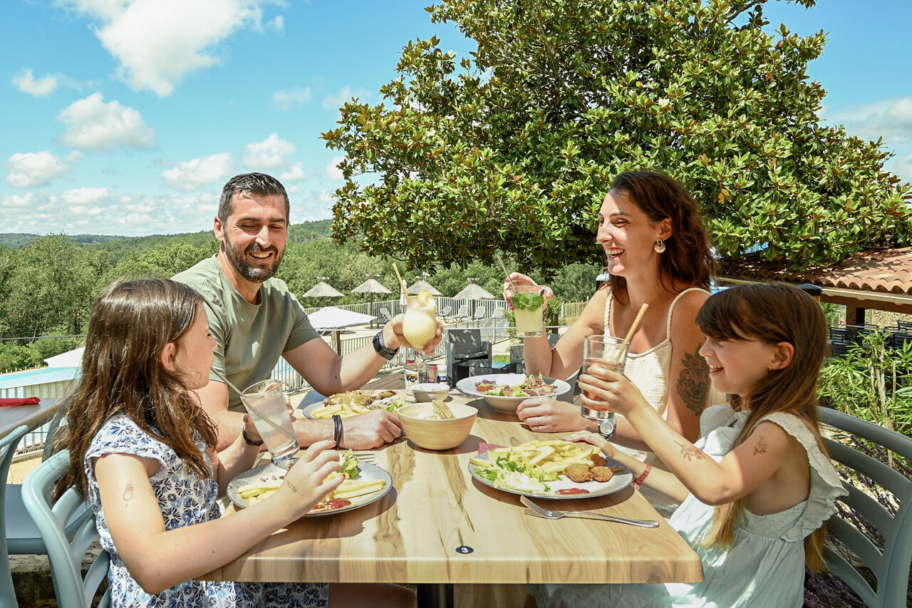 Famille souriante d�jeunant sur la terrasse du restaurant-bar au camping CLICOCHIC Linotte � Le Bugue.