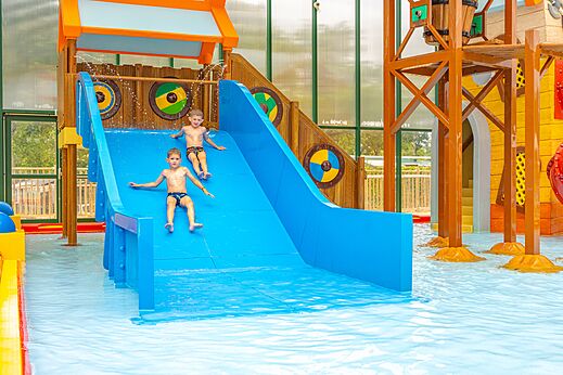 Deux enfants sur toboggan aquatique bleu dans piscine couverte au camping CAPFUN Lodge à SARZEAU (56).