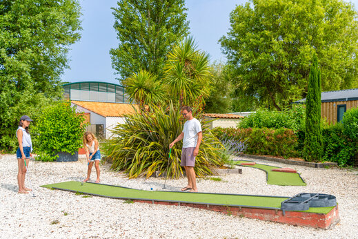 Mini-golf avec famille jouant sur parcours verdoyant au camping CAPFUN Loubine à Les Sables d'Olonne (85).
