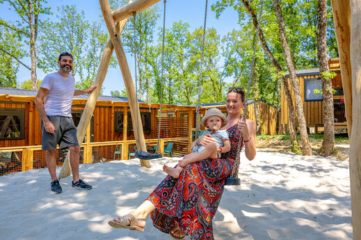 Famille profitant d'une balançoire sur l'aire de jeux avec Mobil-homes au camping CLICOCHIC Lou Castel à Castelnaud-la-Chapelle (24).
