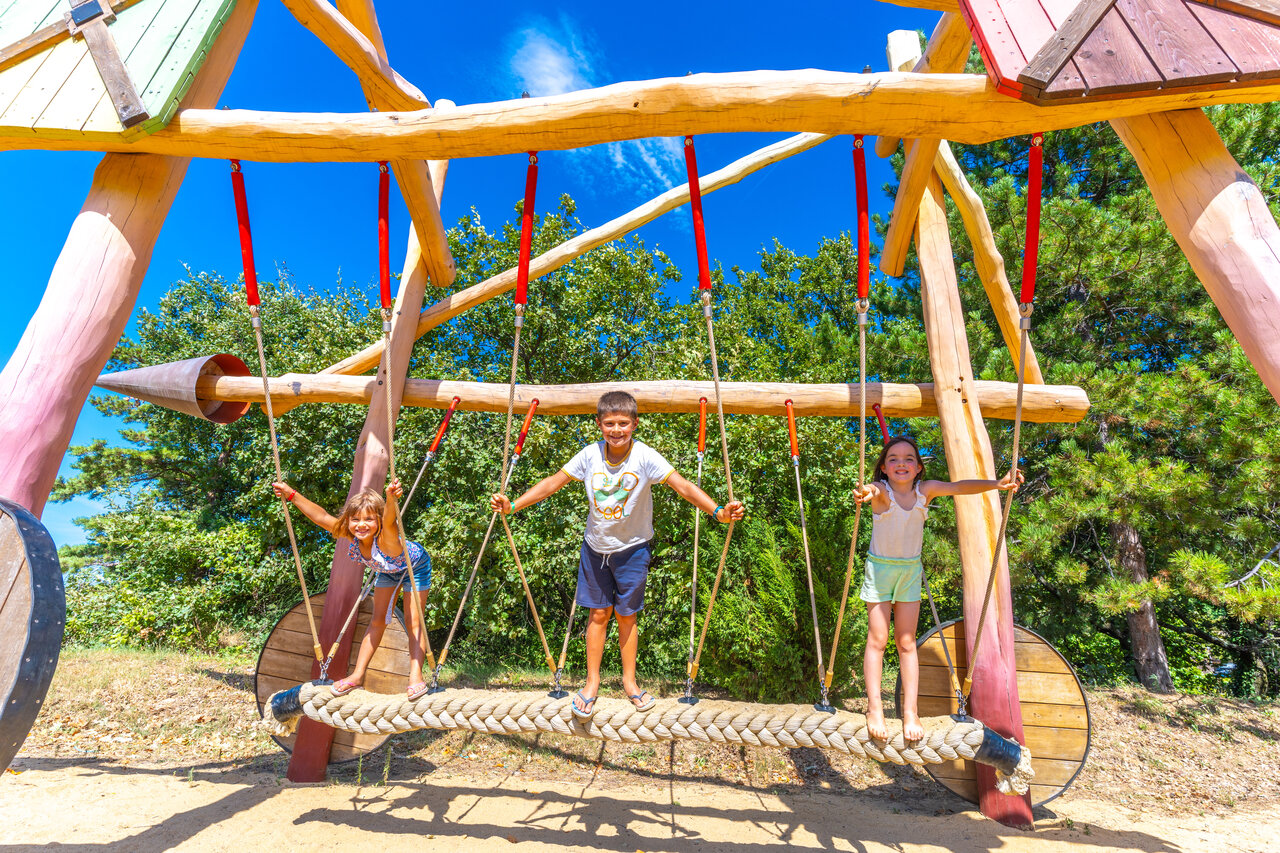 Aire de jeux en bois, enfants souriants au camping CAPFUN Merle Roux (07).