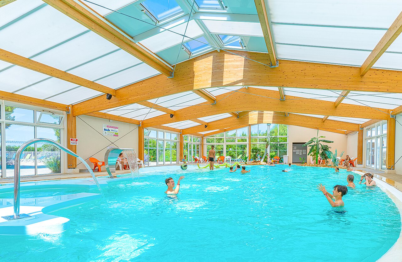 Piscine couverte avec jeux d'eau et baigneurs au camping VAGUES OCEANES Micheli�re � Givrand (85).