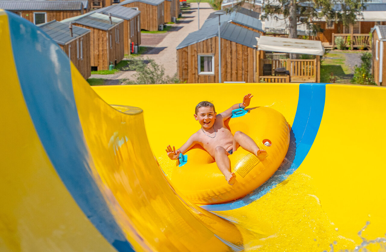 Enfant souriant sur bou�e, toboggan aquatique jaune au camping CAPFUN Palais de Gaufrette.