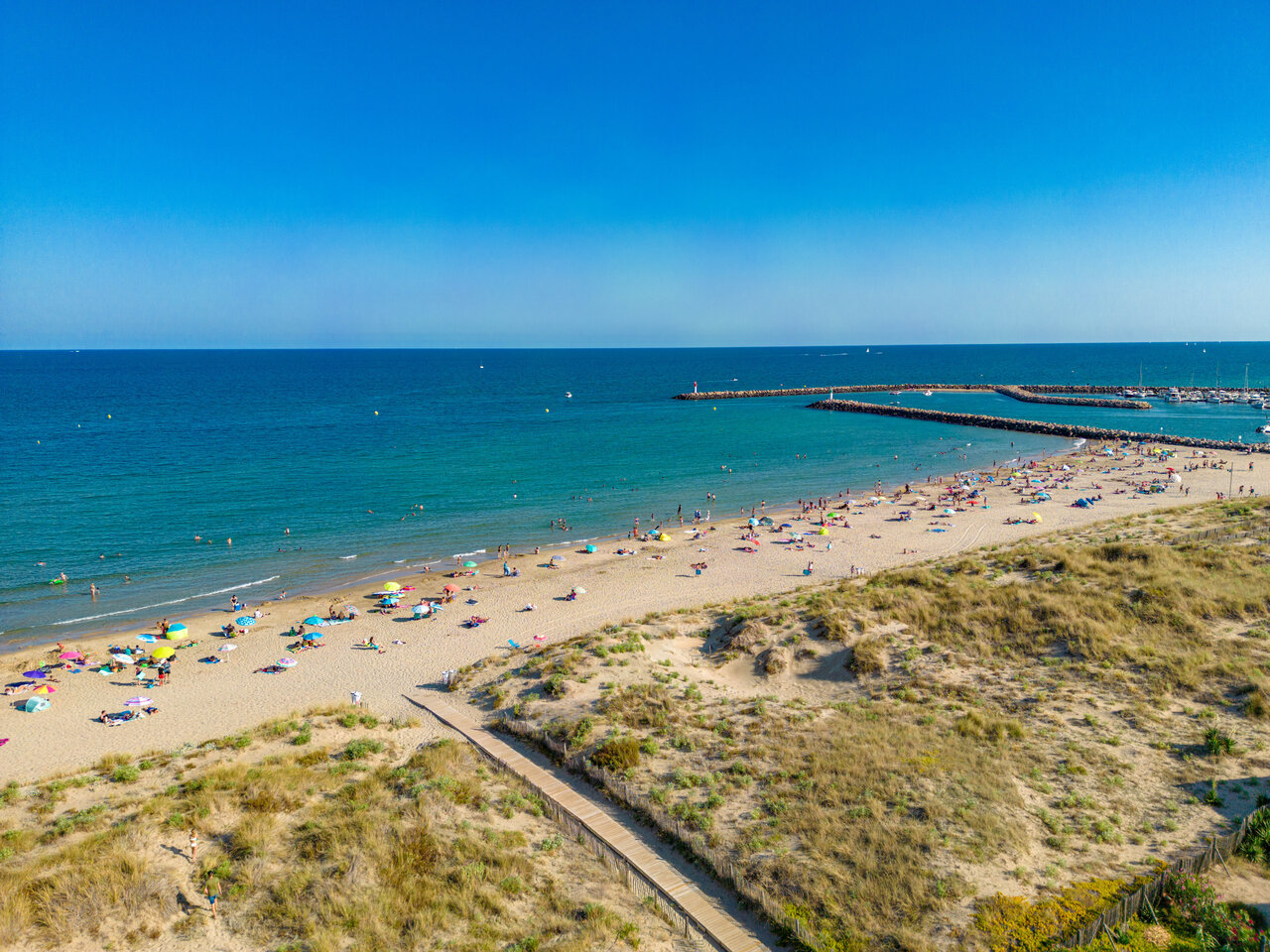 Plage de sable fin, baigneurs et port de plaisance au camping CLICOCHIC Paradou.