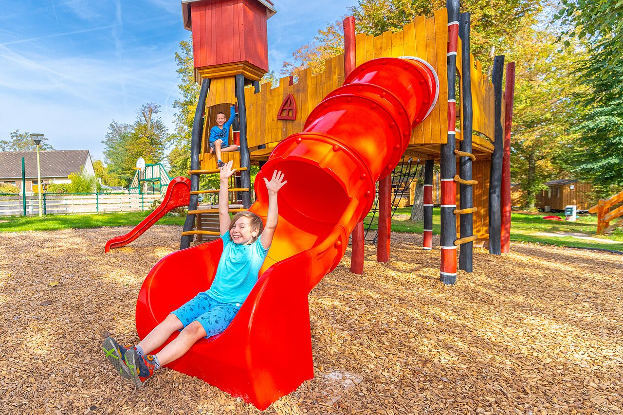 Enfant souriant sur toboggan rouge aire de jeux au camping CAPFUN Parc de Paris � Villevaud� (77).