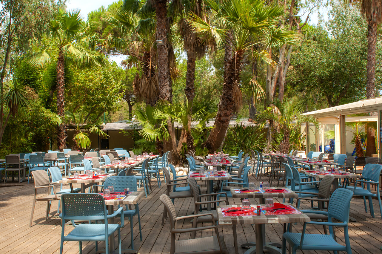 Terrasse de restaurant ext�rieure, tables, palmiers, camping CAPFUN Parc et Plage Hy�res (83).