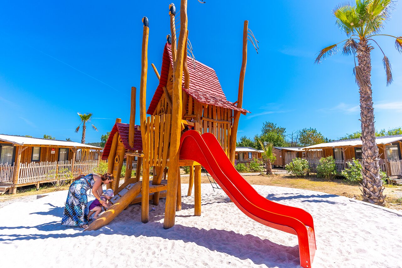 Aire de jeux avec toboggan rouge sur sable au camping CAPFUN La Pin�de de Grimaud.