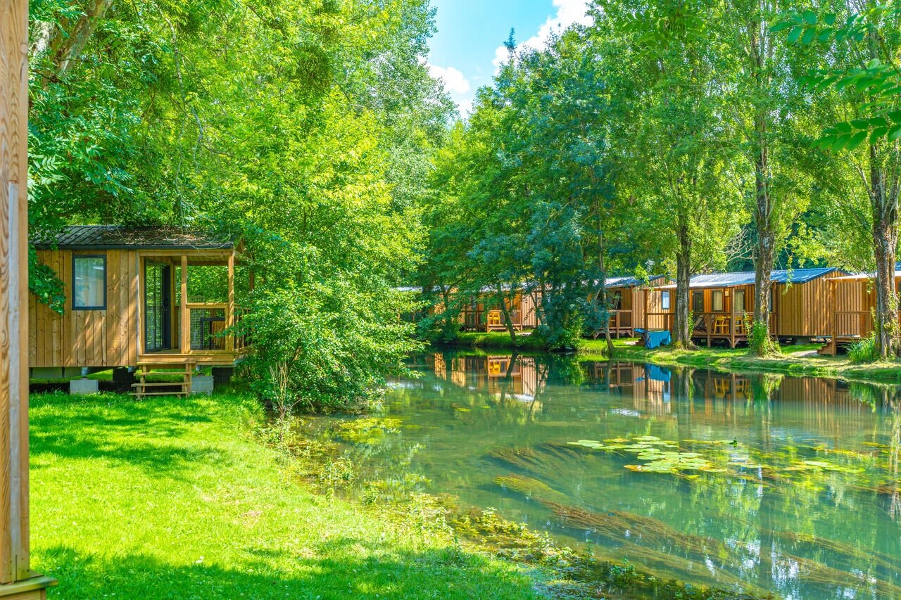 Mobil-homes en bois au bord d'une rivi�re verdoyante, nature luxuriante au camping CAPFUN La Rivi�re � Valence-en-Poitou (86).