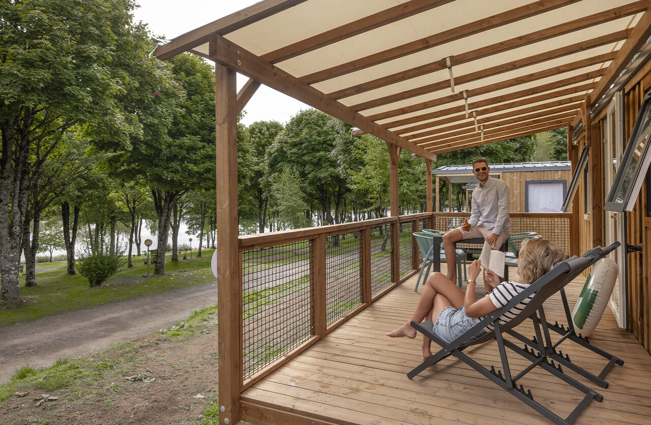 Couple sur terrasse Mobil-home en bois, vue lac, au camping CLICOCHIC Soleil Levant.