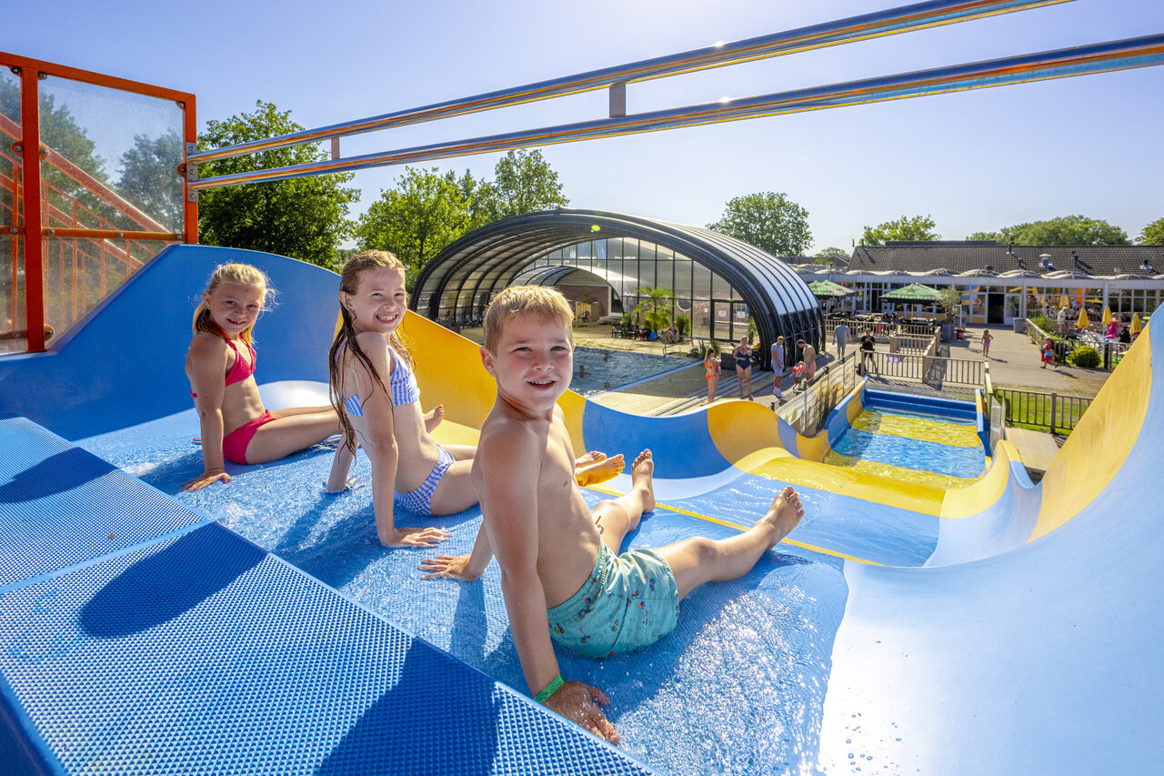 Enfants souriants sur toboggan aquatique bleu et jaune au camping CAPFUN De Sprookjescamping � Rheeze.