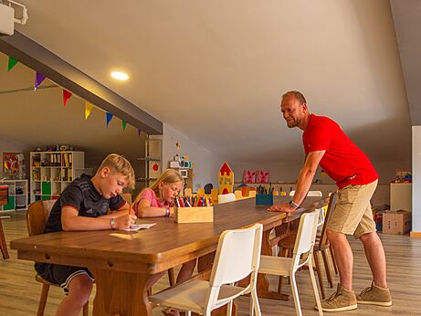 Enfants dessinant à une table avec un animateur au camping CAPFUN Tecklenburg à Tecklenburg-Leeden (49).