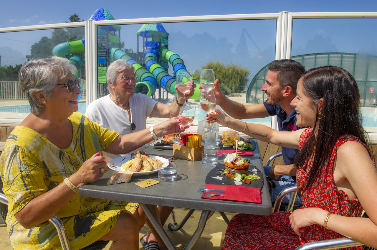 Famille trinquant en terrasse, piscine et toboggans au camping CAPFUN Celeste � Breuillet (17).