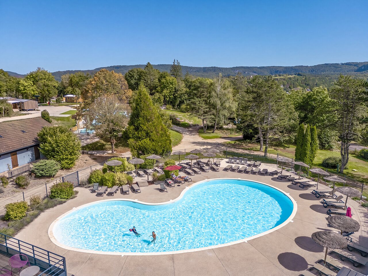 Piscine ext�rieure en forme libre avec chaises et parasols au camping CLICOCHIC Trelachaume � Maisod (39).