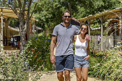 Couple souriant se promenant sur un chemin verdoyant au camping CAPFUN Vignes d'Or à Serignan.
