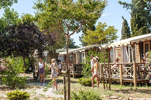 Mobil-homes en bois avec terrasses et personnes jouant au badminton au camping CAPFUN Vignes d'Or à Serignan.