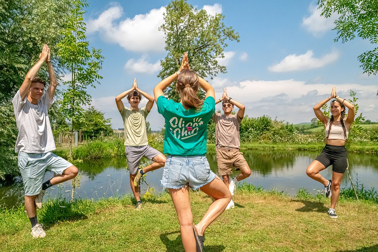 Groupe pratiquant le yoga en plein air pr�s d'un �tang au camping CLICOCHIC Village des Meuniers � Dompierre-les-Ormes.